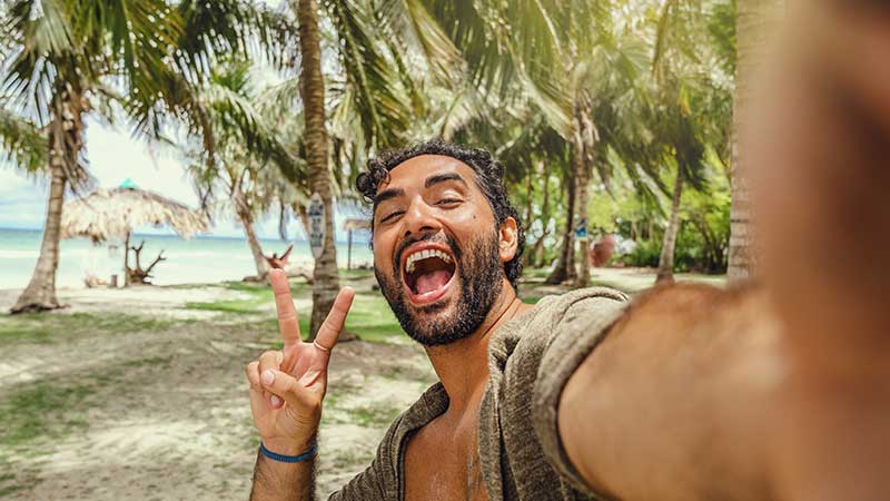 Một người đàn ông đang chụp ảnh selfie ở bãi biển, tận hưởng thời gian du lịch khi sử dụng thẻ tín dụng ở nước ngoài